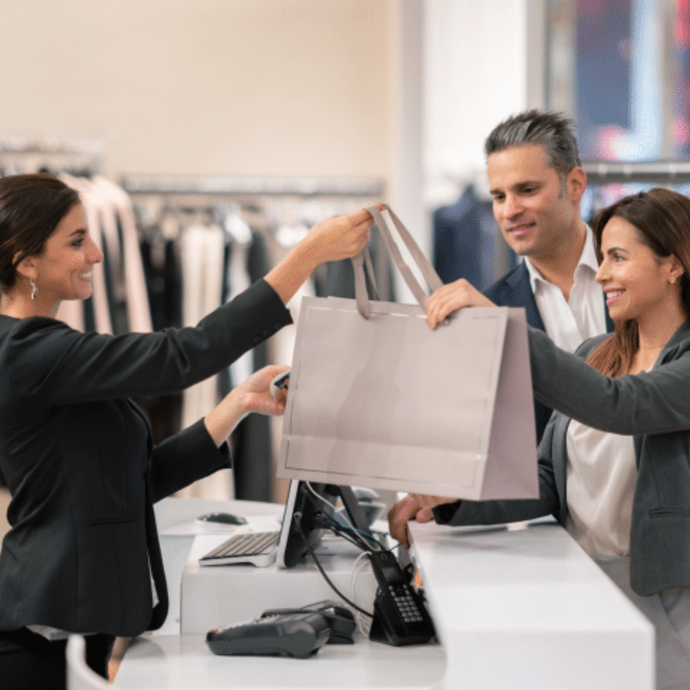 The store employee is wrapping up the items purchased by the customer and handing them over